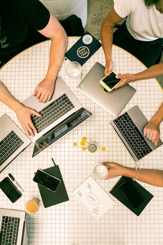 photo-of-people-using-laptop-3194519 Top view of a team collaborating with laptops, phones, and notes in a modern office.